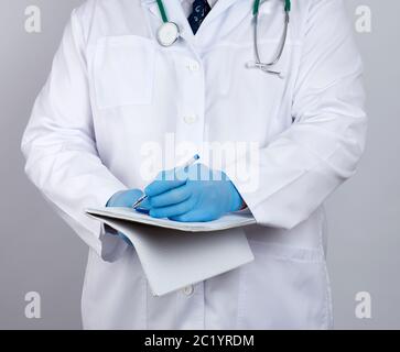 médecin en manteau blanc, les gants stériles en latex bleu contiennent un carnet jaune ouvert dans sa main sur fond blanc, concept d'enregistrement du diagnostic Banque D'Images