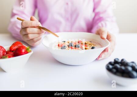 Gros plan de jeunes femmes ayant un repas santé petit déjeuner avec des céréales, des fraises et des bleuets Banque D'Images