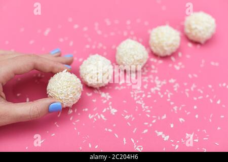 main femelle avec bonbons couverts de noix de coco déchiquetée. boules de noix de coco sur fond rose Banque D'Images