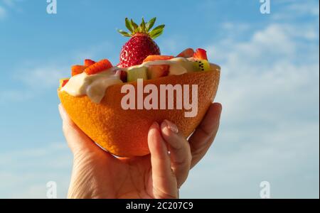 Salade de fruits dans un pot à base de pamplemousse. Nourriture aux fruits dans la main d'une femme. Petit déjeuner sain et diététique. Banque D'Images
