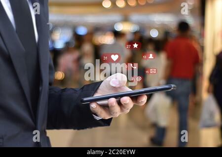 Gros plan sur un homme d'affaires utilisant un smartphone mobile avec des icônes de réseaux sociaux sur un arrière-plan flou de la gare d'aéroport. Entreprise, technologie ou réseau social Banque D'Images