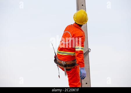 Électriciens en uniforme travaillant sur des poteaux électriques haute tension avec des équipements de sécurité. Banque D'Images