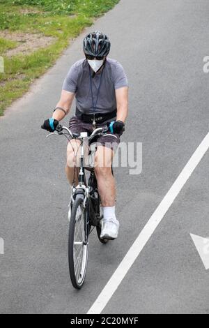 Un homme plus âgé portant un masque et un casque en vélo sur un sentier près de Cross Island Parkway à Bayside, Queens, New York. Banque D'Images