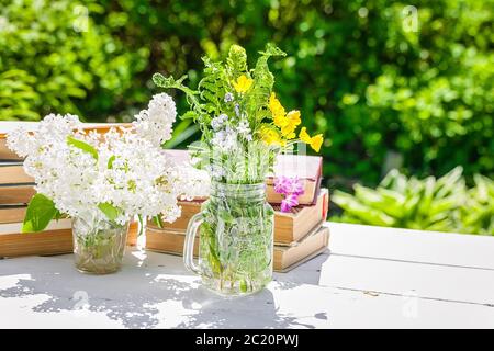 Des piles de vieux livres, une branche de lilas blanc et un bouquet de fleurs d'été sur une table en bois. Composition vintage. Copier l'espace Banque D'Images