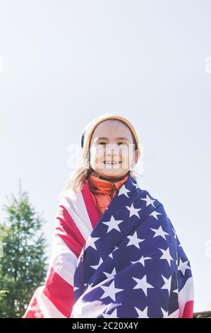 Bonne adolescente tenant le drapeau national des États-Unis. Fond bleu ciel. Journée du drapeau aux États-Unis. Tir vertical Banque D'Images