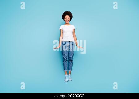 Photo de corps complet de drôle de peau sombre dame ondulée saut haut étonnant ensoleillé jour d'été gai bonne humeur porter décontracté blanc t-shirt jeans chaussures isolées Banque D'Images