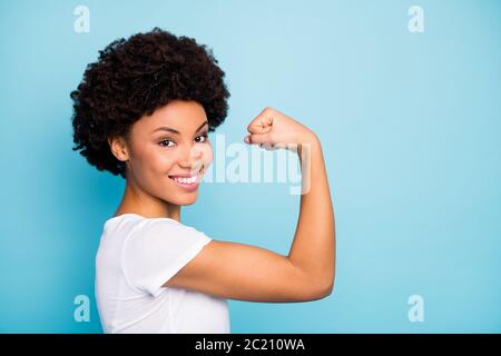 Gros plan photo de profil de belle peau sombre femme en forme de curly montrant la forme parfaite biceps après l'entraînement intense vêtements de gym décontracté blanc t-shirt isolé Banque D'Images