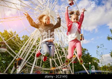 Deux filles s'amusent dans un parc d'attractions. Une grande roue se trouve en arrière-plan. Banque D'Images