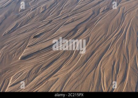 Vue rapprochée en regardant vers le bas sur des motifs dans une plage de sable humide, montrant des textures, des formes et des ondulations Banque D'Images