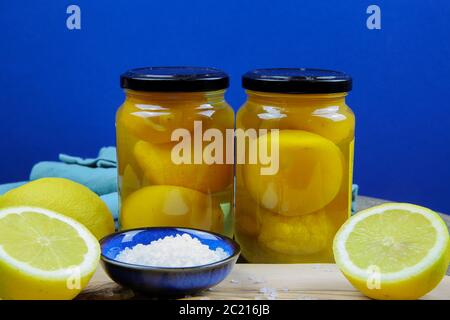 Préparation de citrons salés marinés conservés au maroc : gros plan de tranches isolées d'agrumes jaunes, bol bleu et cuillère en bois avec sa mer épaisse Banque D'Images