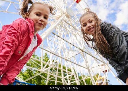 Deux filles s'amusent dans un parc d'attractions. Une grande roue se trouve en arrière-plan. Banque D'Images