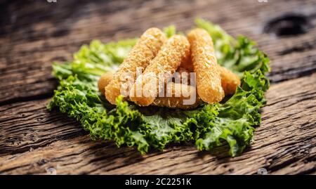 Détail de bâtonnets de mozzarela frits sur une feuille verte placée sur une table en bois rustique Banque D'Images