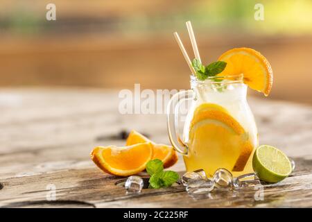Pot rafraîchissant de limonade orange avec glace, menthe, pailles en papier et quartiers d'orange et de citron vert frais sur le côté. Banque D'Images