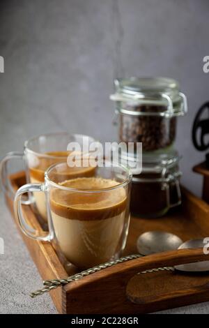 Boisson glacée au café Dalgona sur fond de plateau en bois. Café instantané ou espresso en poudre fouetté avec du sucre et de l'eau chaude. Café avec lait Banque D'Images