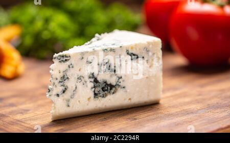 Tranche de fromage bleu sur une planche à découper avec des légumes en arrière-plan Banque D'Images
