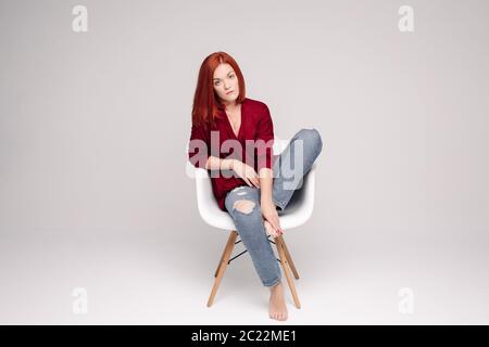 Modèle avec cheveux gingembre assis sur chaise blanche en studio. Banque D'Images