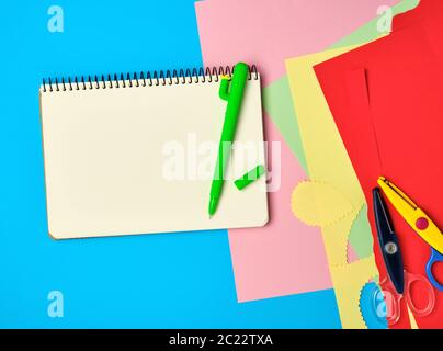 carnet blanc carré, stylo vert et ciseaux sur fond bleu, retour à l'école Banque D'Images