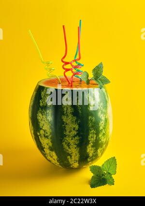 Rayé mûre pastèque vert est coupé et cocktail en plastique multicolore tubes avec une feuille de menthe sur fond jaune, cocktail rafraîchissant Banque D'Images