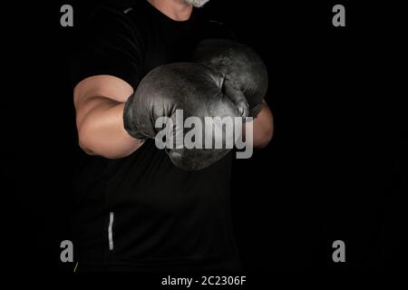 Jeune homme se trouve dans un rack de boxe, en tenue très old vintage black boxing gloves sur ses mains, fond sombre Banque D'Images