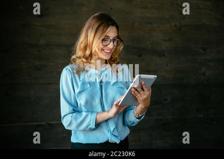Charmant jeune businesswoman using a tablet, dactylographie, chercher quelque chose. Vêtu d'un élégant chemisier, dans les lunettes. Banque D'Images