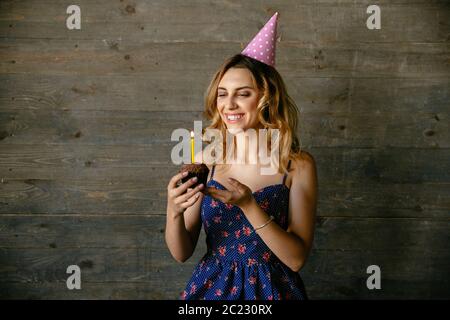 Happy attractive girl chocolate cupcake, célébrer son propre anniversaire. Habillé en robe bleue, en chapeau de fête. Vacances concept. Banque D'Images