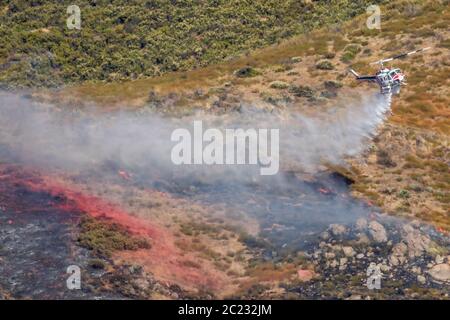 Winchester, CA USA - 14 juin 2020 : l'hélicoptère CAL Fire dépose de l'eau sur un feu de forêt sec au sommet d'une colline près de Winchester, en Californie. Banque D'Images