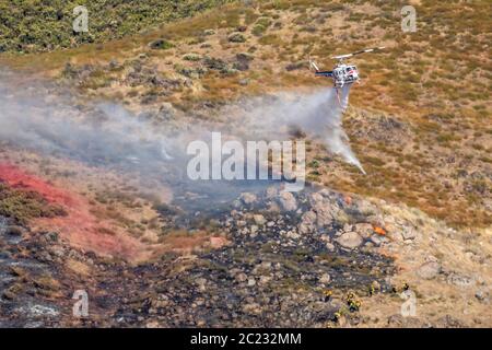 Winchester, CA USA - 14 juin 2020 : l'hélicoptère CAL Fire dépose de l'eau sur un feu de forêt sec au sommet d'une colline près de Winchester, en Californie. Banque D'Images