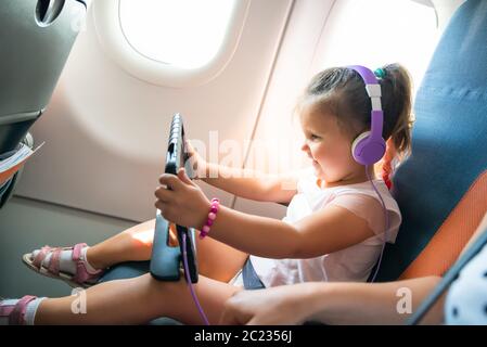 Adorable petite fille avec casque sur la tête à l'aide de tablette numérique lors de voyages en avion Banque D'Images