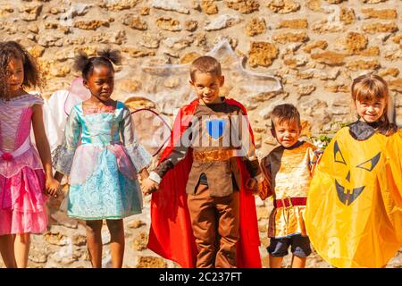 Rangée d'enfants en costumes d'Halloween tiennent les mains sur le mur de pierre Banque D'Images