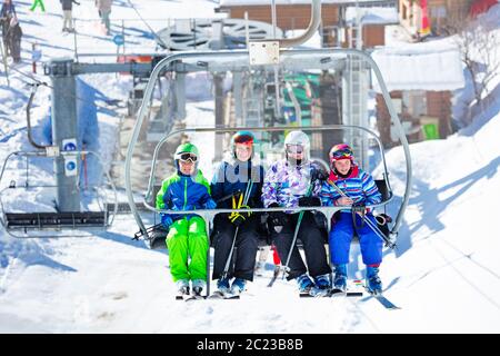 Quatre enfants, garçons et filles, s'assoient ensemble sur le télésiège de la montagne avec la gare derrière Banque D'Images