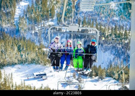 Quatre amis enfants s'assoient ensemble sur un télésiège sur la montagne avec forêt verte en dessous Banque D'Images