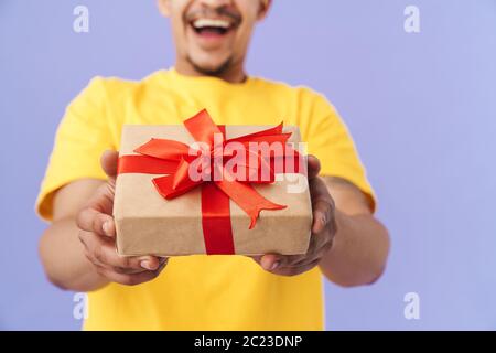 Photo rognée d'un homme afro-américain heureux tenant une boîte cadeau et souriant isolé sur fond violet Banque D'Images