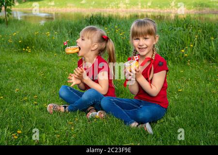 Concept de la fête du Canada heureuse. Deux filles de race blanche avec des beignets célébrant à l'extérieur de l'Anniverasy canadienne. Banque D'Images