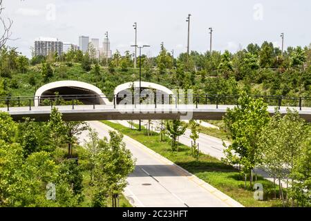 Vue sur le tunnel de l'autoroute et le passage supérieur piéton près du parc et de la rivière Arkansas avec des arbres et des fleurs sauvages nouvellement plantés et des gratte-ciel de Tulsa in Banque D'Images