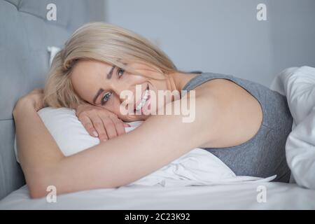 Smiling casual blonde couché dans son lit dans la chambre à coucher Banque D'Images
