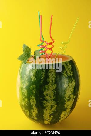 Rayé mûre pastèque vert est coupé et cocktail en plastique multicolore tubes avec une feuille de menthe sur fond jaune, cocktail rafraîchissant Banque D'Images