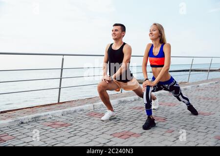 Sur toute la longueur du bel homme qu'une jolie femme faisant des exercices d'étirement des jambes, au cours de l'entraînement sur le quai, près de la mer. Banque D'Images