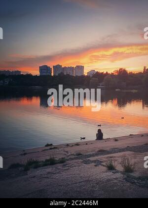 Scène nocturne idyllique et Moody avec une petite silhouette de fille, nourrissant les canards sauvages, assis près du lac dans le parc. Magnifique coucher de soleil d'été avec Banque D'Images