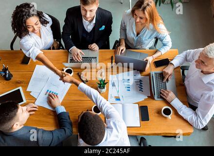 Collègues qui se secouent pendant une réunion assis dans un bureau moderne, vue de dessus Banque D'Images