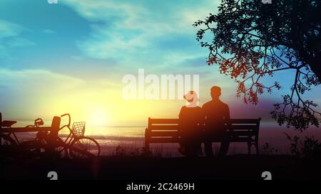 Silhouettes d'un couple assis sur un banc et regardant le soleil couchant sur l'océan. Banque D'Images