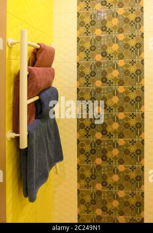 Salle de bains vide avec mur de douche gris derrière un porte-serviette en métal blanc avec des serviettes pliées sur le dessus Banque D'Images