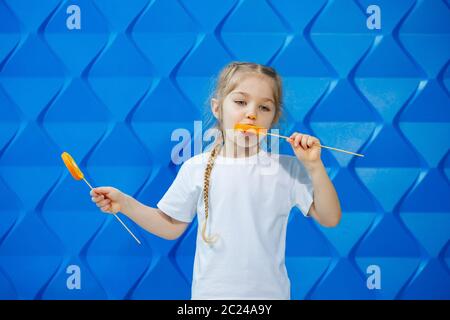 Jolie fille aux oranges, elle les mange sur fond bleu Banque D'Images