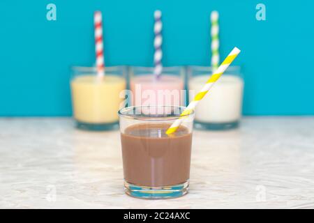 Milkshake au chocolat avec une paille papier rétro en face d'une rangée de milkshakes et lait frais contre un arrière-plan bleu sarcelle Banque D'Images