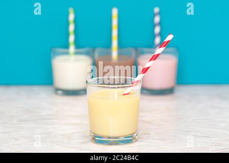 Milkshake banane avec une paille papier rétro en face d'une rangée de lait frais et aromatisé de lait frappé contre un arrière-plan bleu sarcelle Banque D'Images