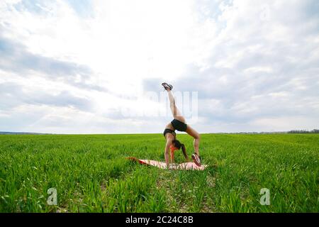 Une jeune femme en haut et short noirs exécute une main. Un modèle se tient sur ses mains, faisant des fractionnements de gymnastique contre le ciel bleu. Un mode de vie sain Banque D'Images