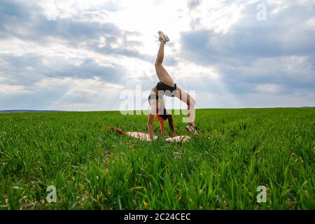 Une jeune femme en haut et short noirs exécute une main. Un modèle se tient sur ses mains, faisant des fractionnements de gymnastique contre le ciel bleu. Un mode de vie sain Banque D'Images