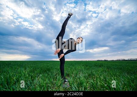 belle fille modèle sur l'herbe verte faire du yoga. Une belle brunette sur une pelouse verte exécute des éléments acrobatiques. La gymnaste flexible en noir fait le exeur Banque D'Images