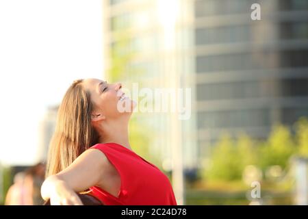 Side view portrait of a happy woman in red, respirant profondément l'air frais assis sur un banc dans la rue Banque D'Images