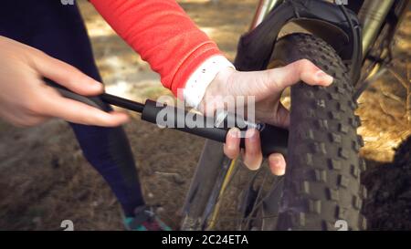 Jeune femme caucasienne athlète cycliste utilise un outil à main, une pompe à vélo pour gonfler l'air dans un pneu roue VTT. B Banque D'Images