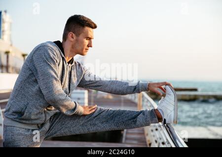 Vue latérale photo de jeune homme motivé dans le sportswear , faisant des exercices d'entraînement pour les jambes, le front de mer. Banque D'Images